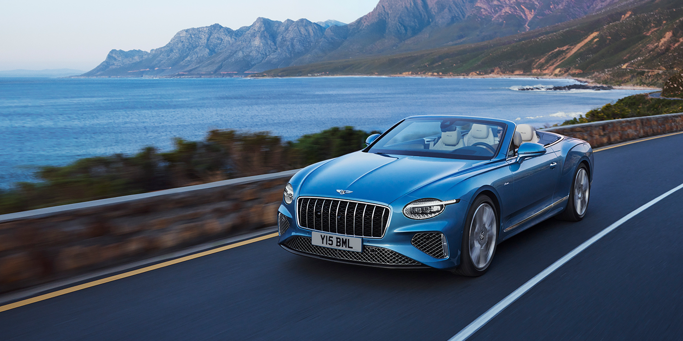 Bentley Porto New Bentley Continental GTC Azure convertible in Light Windsor blue paint with 22 inch Azure wheels and chrome grill, driving dynamically by the sea