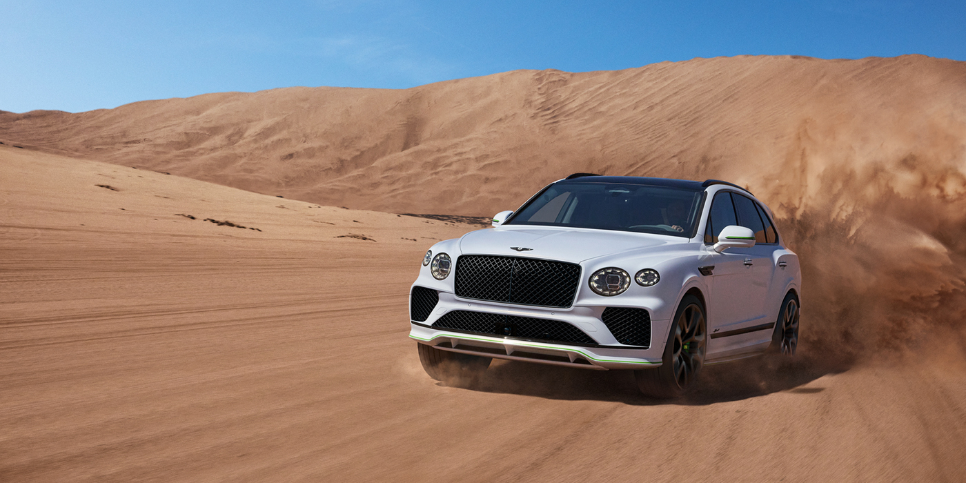 Bentley Porto Bentley Bentayga Speed SUV front three quarter in Snow Quarts Pearlescent by Mulliner white paint driving dynamically through the desert