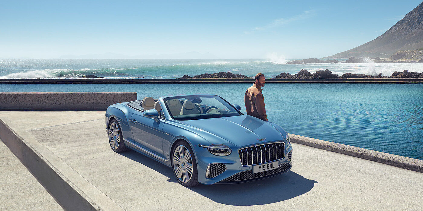 Bentley Porto New Bentley Continental GTC Azure convertible front view in Light Windsor blue paint with 22 inch ten spoke wheels parked by the sea in the sunshine