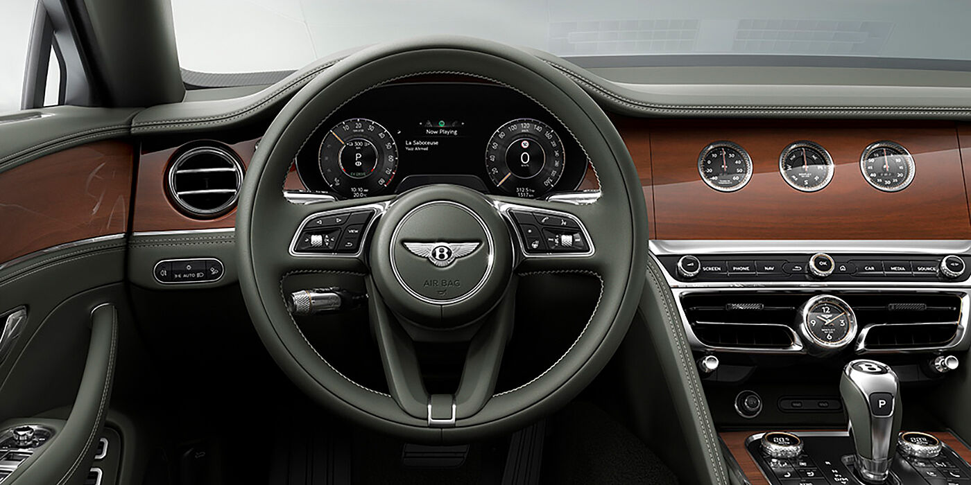 Bentley Porto New Bentley Flying Spur sedan front cabin in Cumbrian Green hide and Crown Cut walnut veneer showing steering wheel and Rotating Display with three clocks on face