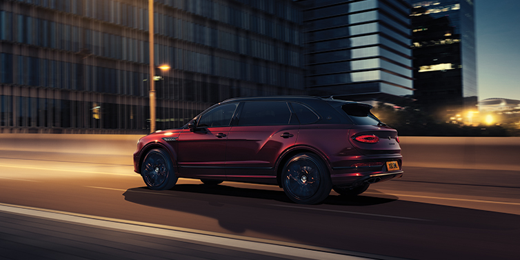 Bentley Porto Bentley Bentayga Extended Wheelbase Mulliner SUV in Cricket Ball red paint driving dynamically in city at night